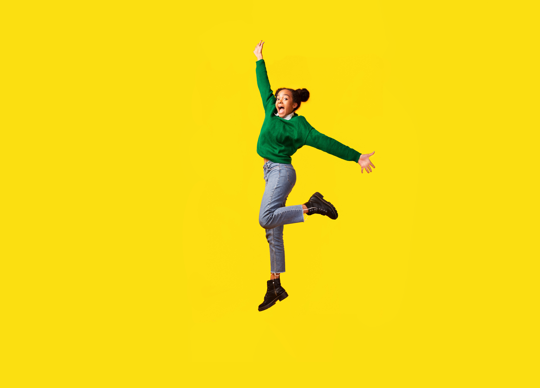Happy afro girl jumps over yellow studio background